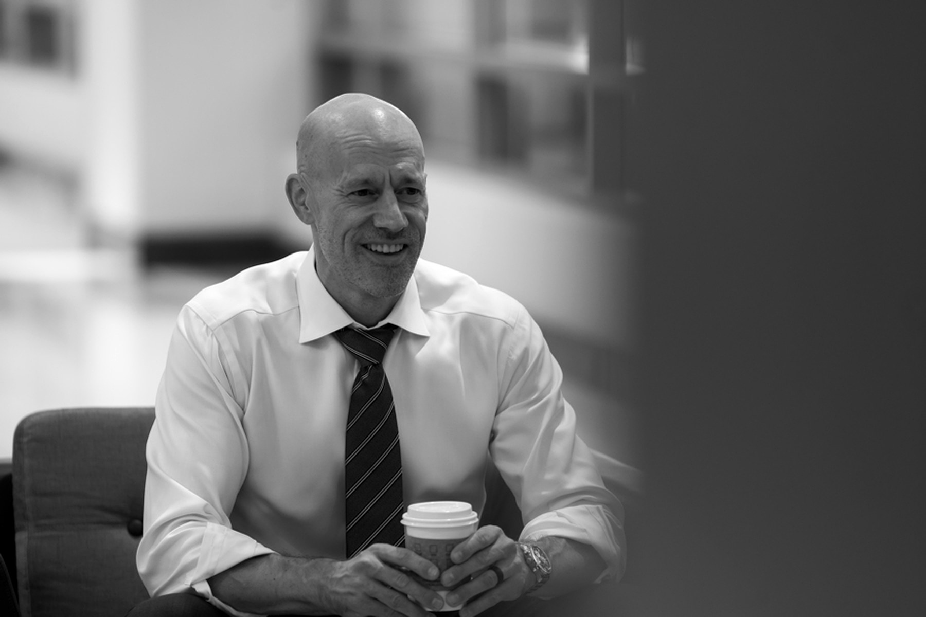 David Sugden seated in shirtsleeves holding a coffee, mid-conversation